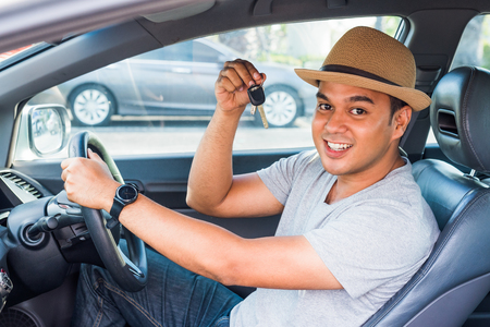 Young asian man holding key while sitting in new carの写真素材