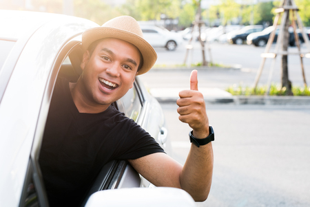 Young asian man showing thumbs up while driving car.