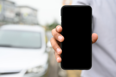 Close up male hand showing blank screen of smartphone on car background.の写真素材