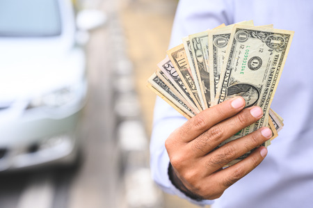 Businessman holding cash in the hand on car background.の写真素材