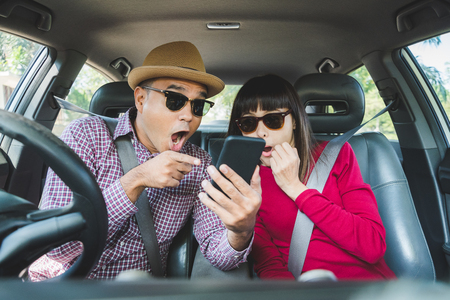 Couple asian man and woman sitting in car and looking at smartphone feel shocked . Travel concept.の写真素材