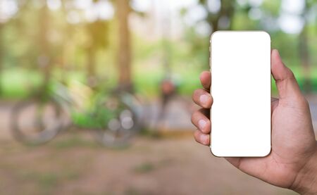 Close up male hand holding smartphone blank screen on park background.