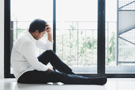 Young asian man sitting in the dark room hand in head feeling depressed, lonely, dramatic and sad.の写真素材