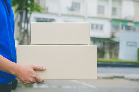 Close up Delivery man in blue uniforms holding parcel cardboard box.