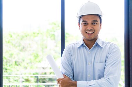Young asian engineer or architects holding layout plan of building.