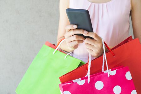 Close up of woman hand holding smartphone and shopping bags.の写真素材