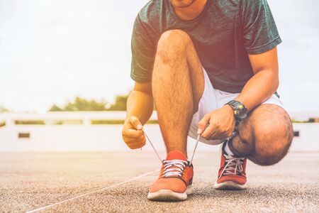 Runner young man tying shoelace getting ready for race on run track.