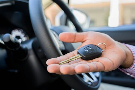 Close up male hand showing car key while sitting in car.