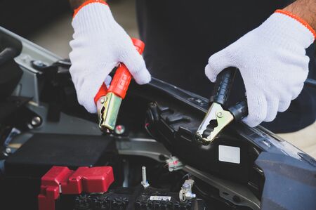 Car mechanic holding  jumper cables for charging a discharged car battery