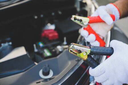 Car mechanic holding  jumper cables for charging a discharged car batteryの写真素材