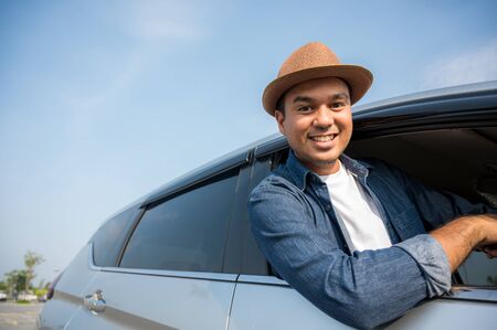 An Asian man is enjoying his trip. He stretches out of the car window to make him look happy.