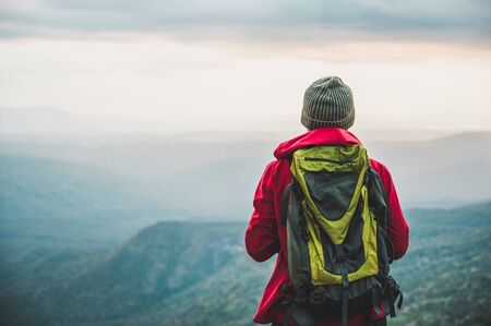 Hikers climbing a red rain jacket carrying a backpack Standing on the edge of a cliff See the beauty of the mountains at sunset, showing success, freedom and adventure.の写真素材