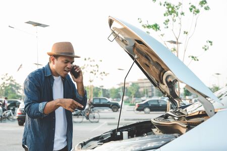 A young Asian tourist has driven a car and broke down on the way. He came down to look at the hood and then called the mechanic for help.の写真素材