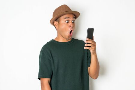 Asian men are using smartphones. He looks at the phone Then made a very surprised face He wears an old green shirt and wears a brown hat. He is around 27-35 years old.の写真素材