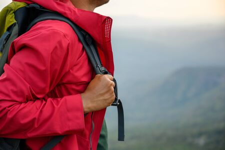 Hikers climbing a red rain jacket carrying a backpack Standing on the edge of a cliff See the beauty of the mountains at sunset, showing success, freedom and adventure.の写真素材
