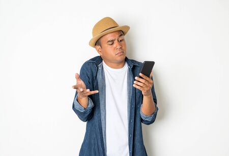 An Asian man is confused with his smartphone. He is about 30-35 years old. He wears a denim shirt.の写真素材