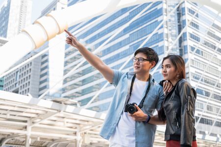 Asian couple tourist looking and pointing finger forward for direction and travel in urban city.