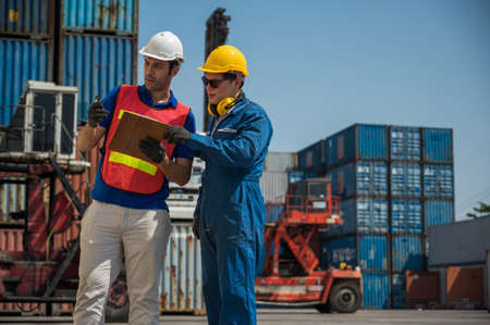 Foreman and dock worker staff working checking at Container cargo harbor holding clipboard. Business...