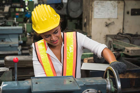Female industrial worker working and checking machine in a large industrial factory with many...