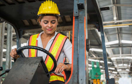 Female industrial worker working and checking machine in a large industrial factory with many...