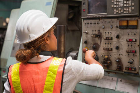 Female industrial worker working and checking machine in a large industrial factory with many equipment.の写真素材