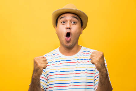 Happy young asian man celebrates with two hand in the air on yellow background.の写真素材