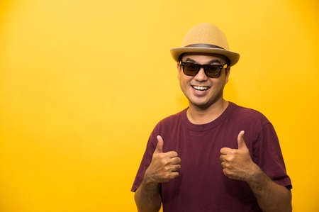 Young Asian man with hat feels happy  and surprise and showing thumb up on yellow background.の写真素材