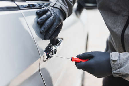 The thief uses a screwdriver Stealing a car at the door handle. The vehicle insurance concept.