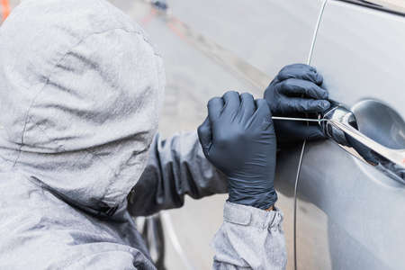The thief uses a screwdriver Stealing a car at the door handle. The vehicle insurance concept.