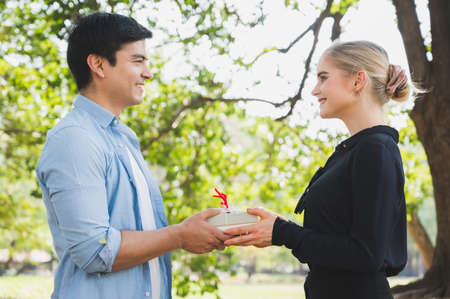Young couple lovers giving a gift box in the park Romantically.の写真素材
