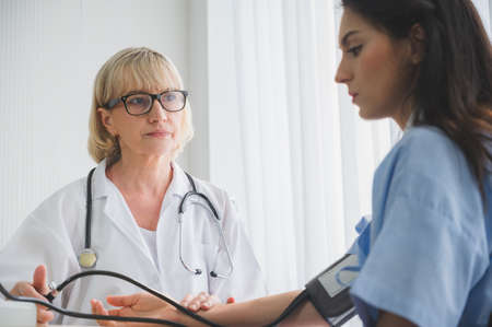 Senior woman doctor checking young female patient blood pressure.の写真素材