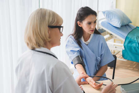 Senior woman doctor checking young female patient blood pressure.の写真素材