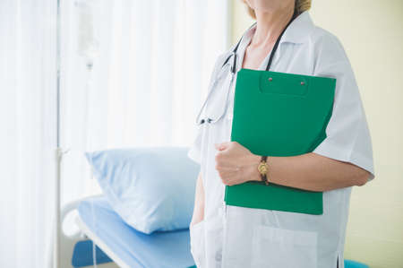 Senior woman doctor with clipboard standing near patient bed. Medical healthcare and doctor service...