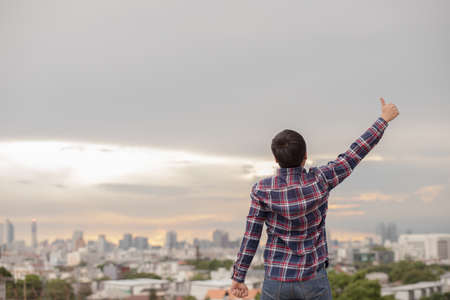 Rear View of asian man showing thumb up in the sky on city view at rooftop.の写真素材