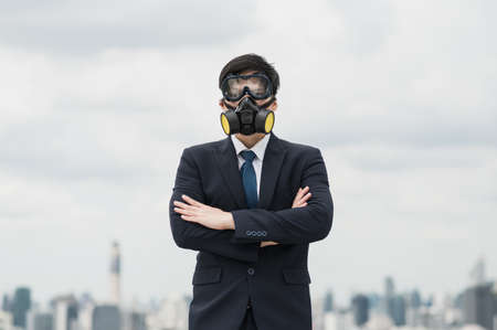 Young handsome asian businessman standing with arms crossed wearing gas mask of protect the...