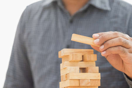 Close up male hand holding arranging or pick up the block wood game and stacking. Growth of Business financial investment and bankrupt concept.の写真素材