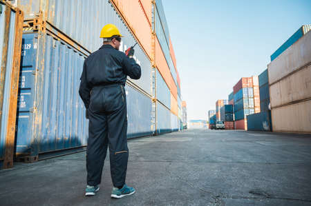 Foreman worker working checking at Container cargo harbor holding radio walkie-talkie to loading containers. Dock male staff business Logistics import export shipping concept.の写真素材