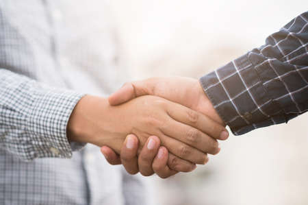 Two men shaking hands to dealing success agreement business. Business people wearing scott shirt on city view background.の写真素材