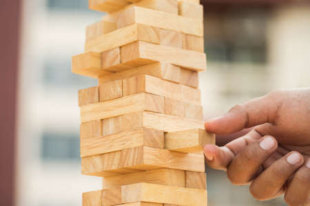 Close up male hand holding arranging or pick up the block wood game and stacking. Growth of Business financial investment and bankrupt concept.の写真素材