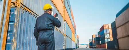 Foreman worker working checking at Container cargo harbor holding radio walkie-talkie to loading...
