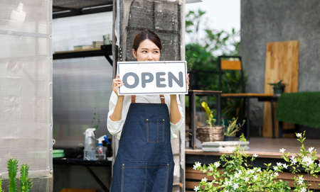 The owner of the tree shop holds a open sign after a long time closed. Cute asian gardener small business open her shop selling small tree for decoration in greenhouse.の写真素材