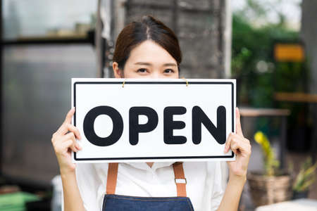 The owner of the tree shop holds a open sign after a long time closed. Cute asian gardener small business open her shop selling small tree for decoration in greenhouse.の写真素材