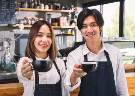 Two asian coffee waitress making cup of hot coffee latte in coffee shop cafe. Barista working with...