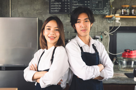 Couple asian barista owner coffee shop standing at counter welcome the customer. Cheerful two young barista man and woman in apron serving cup of hot coffee in cafe.の写真素材