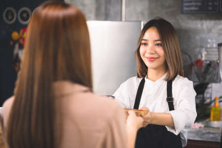 A customer orders a hot latte to the barista. Asian Staff coffee shop cafe making hot coffee and serve to customer. Small business sme concept.の写真素材