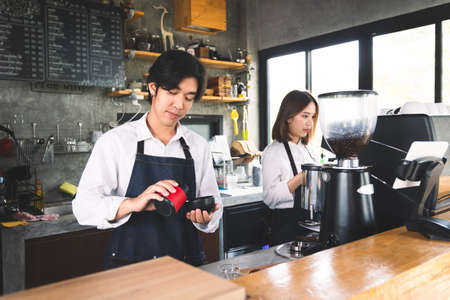 Two asian coffee waitress making cup of hot coffee latte in coffee shop cafe. Barista working with coffee machine in shop.の写真素材