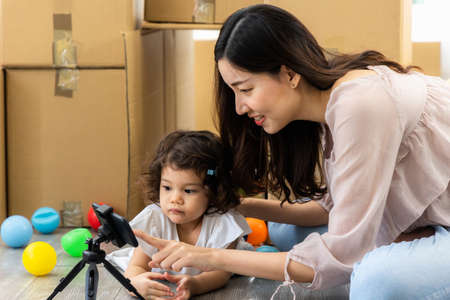 Family relaxing in living room at home. Mom and daughter smartphone watching movies, play game and video conference in the house. Digital Lifestyle Concept.の写真素材