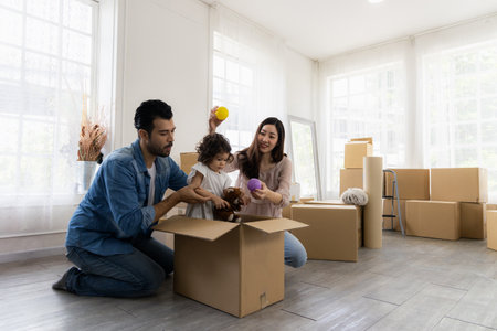 Daughter sits in a carton paper box playing with dad and mom. The family just moved to a new home. Parents and children have fun organizing things together.の写真素材