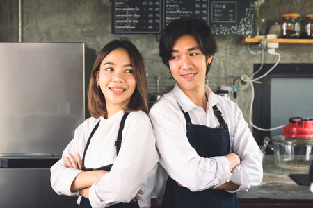 Couple asian barista owner coffee shop standing at counter welcome the customer. Cheerful two young barista man and woman in apron serving cup of hot coffee in cafe.の写真素材