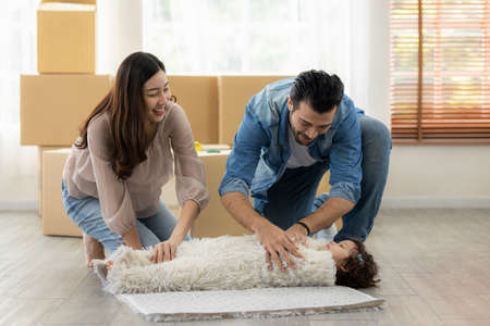 Family relaxing at home. Father mother and daughter help clean the house. Helping roll carpet together.の写真素材